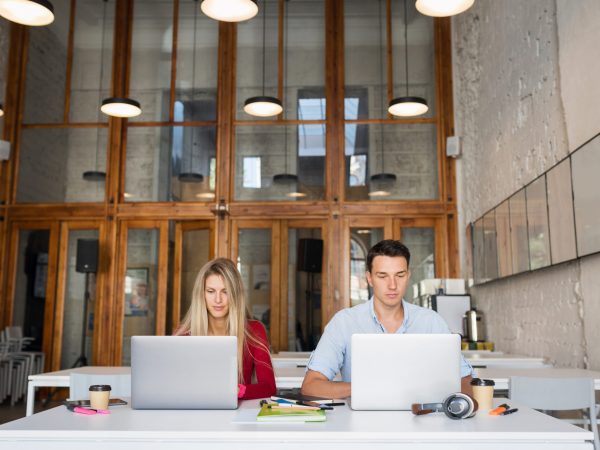 young man and woman working on laptop in open space co-working office room, busy freelancers